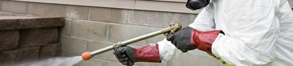 Pest control technician applying exterior insect treatment along a home foundation in Oakland, CA