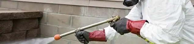 Pest control technician applying exterior insect treatment along a home foundation in Oakland, CA