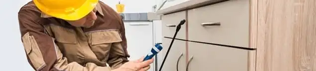 Roach exterminator applying treatment under kitchen cabinets in Oakland, CA