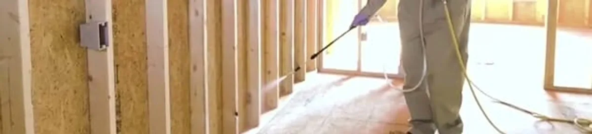 Termite treatment technician applying spray along framing and unfinished walls in Oakland, CA