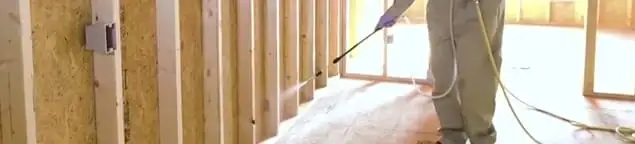 Termite treatment technician applying spray along framing and unfinished walls in Oakland, CA